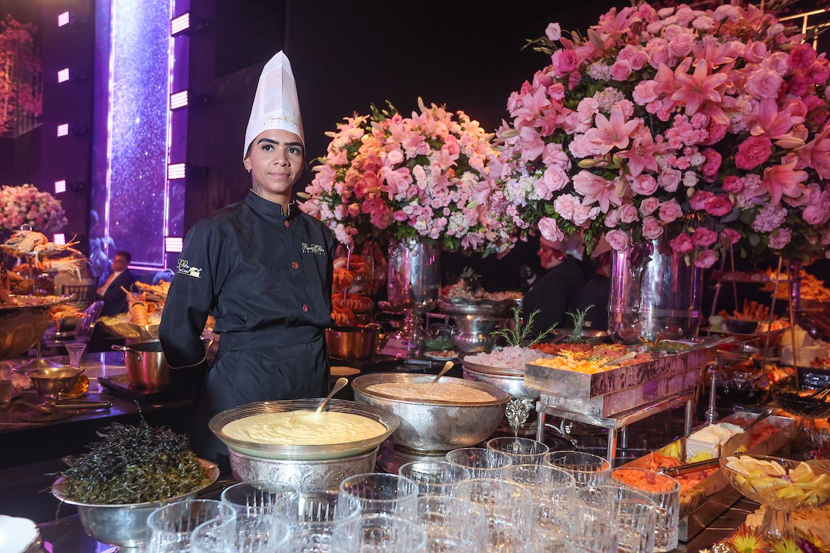 Mulher com traje gastronômico atrás de mesa de buffet em festa - Metrópoles