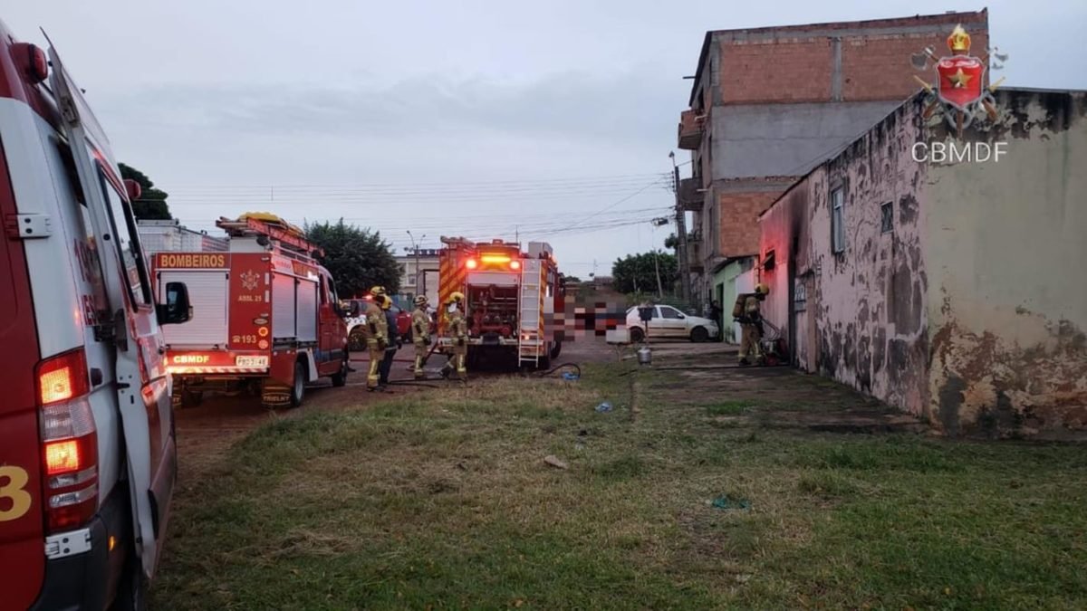 Dois caminhões de bombeiro e uma ambulância em frente à casa após apagadas chamas do incêndio.