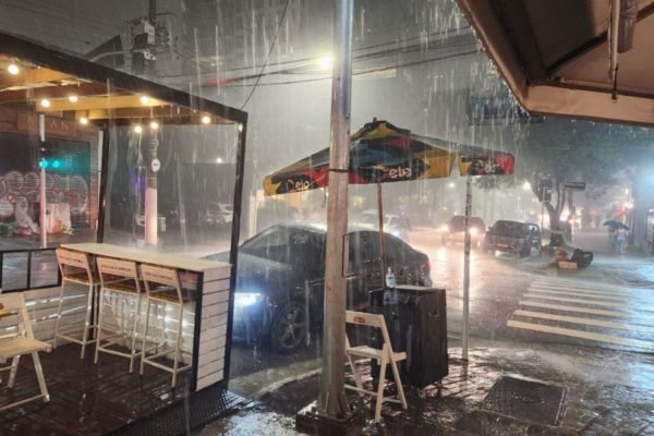 Imagem colorida mostra rua sob forte chuva em São Paulo, com carro estacionado e guarda chuva de vallet - Metrópoles