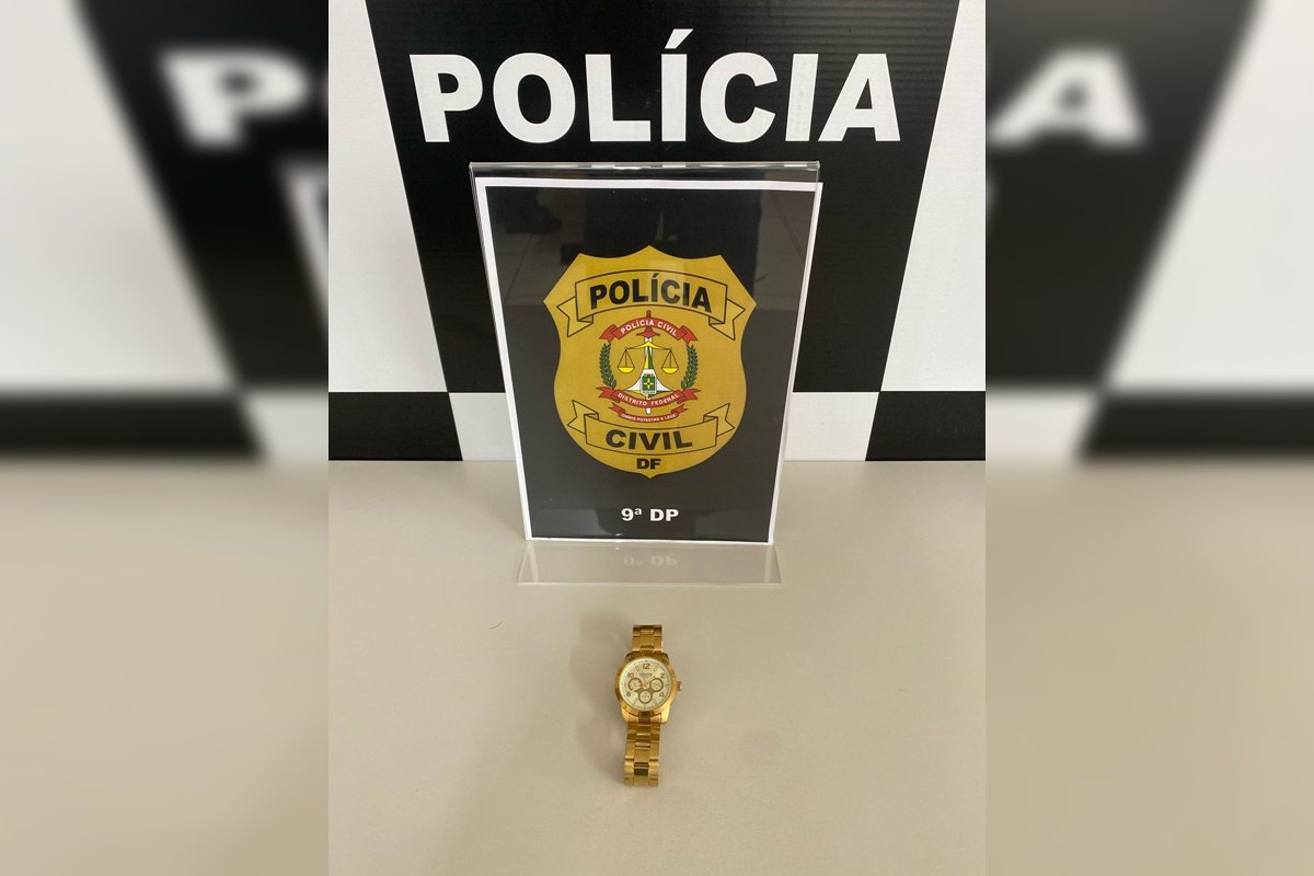 Relógio de pulso de luxo dourado em frente a banner da Polícia Civil