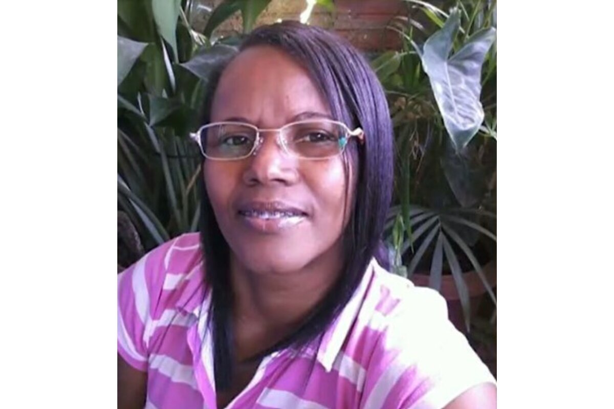 Mulher parda e cabelo liso em frente a planta usando camiseta estilo polo listrada de rosa e branco - Metrópoles