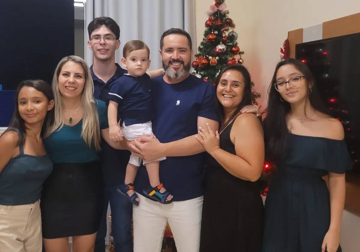 Foto colorida de uma família reunida em frente a uma árvore de Natal - Metrópoles