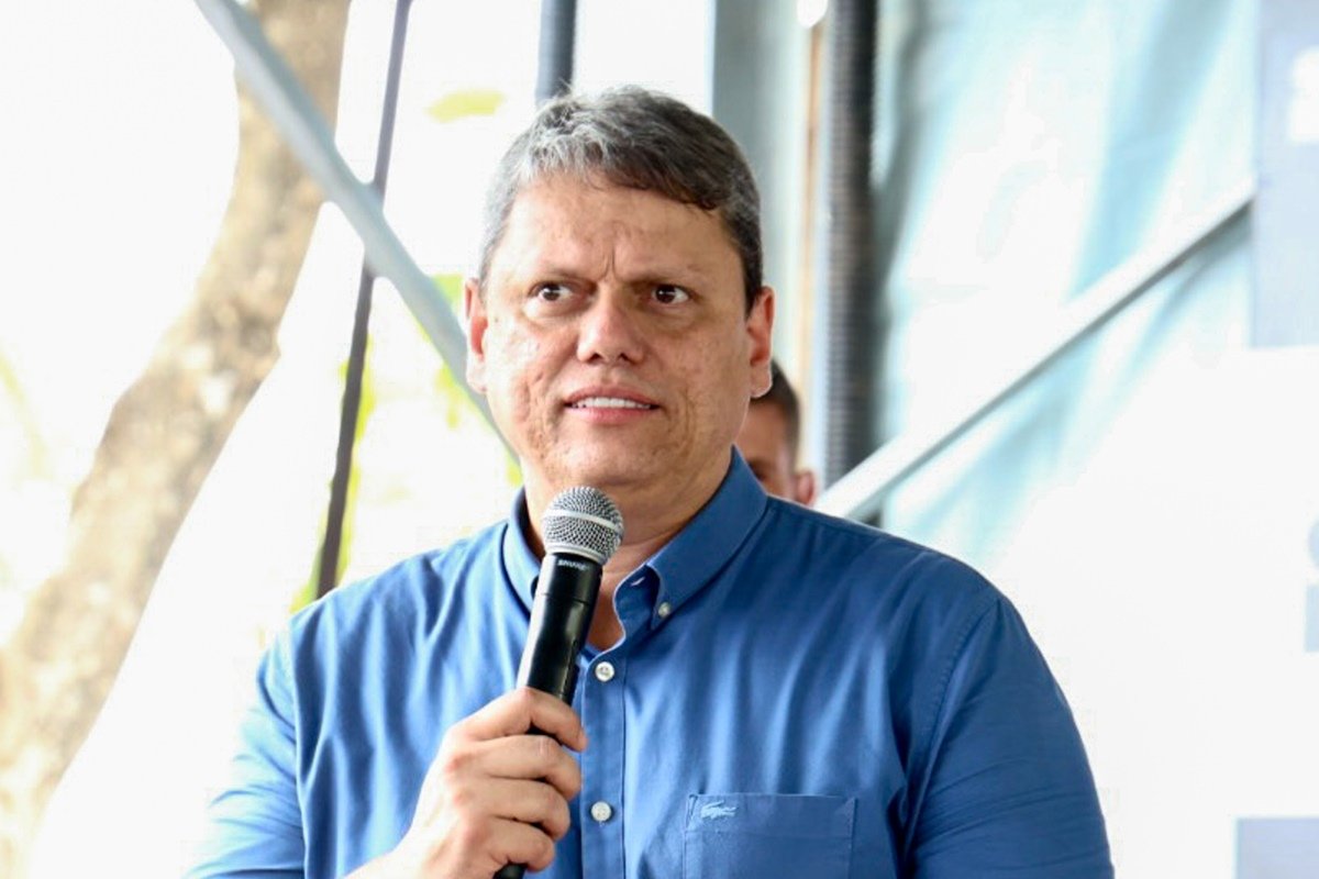 Imagem colorida mostra Tarcísio de Freitas, homem branco e grisalho, de camisa azul, falando ao microfone - metrópoles