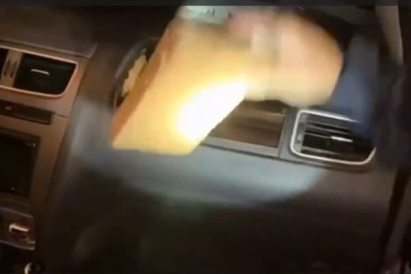 Imagem colorida mostra agente da PRF retirando pacote de cocaína de compartimento de air bag de um carro no interior de SP - Metrópoles