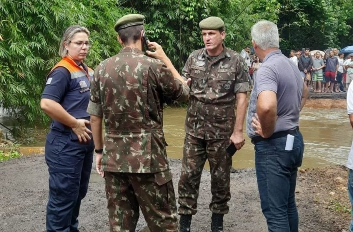 Um homem com traje militar fala ao telefone enquanto as outras pessoas o encaram