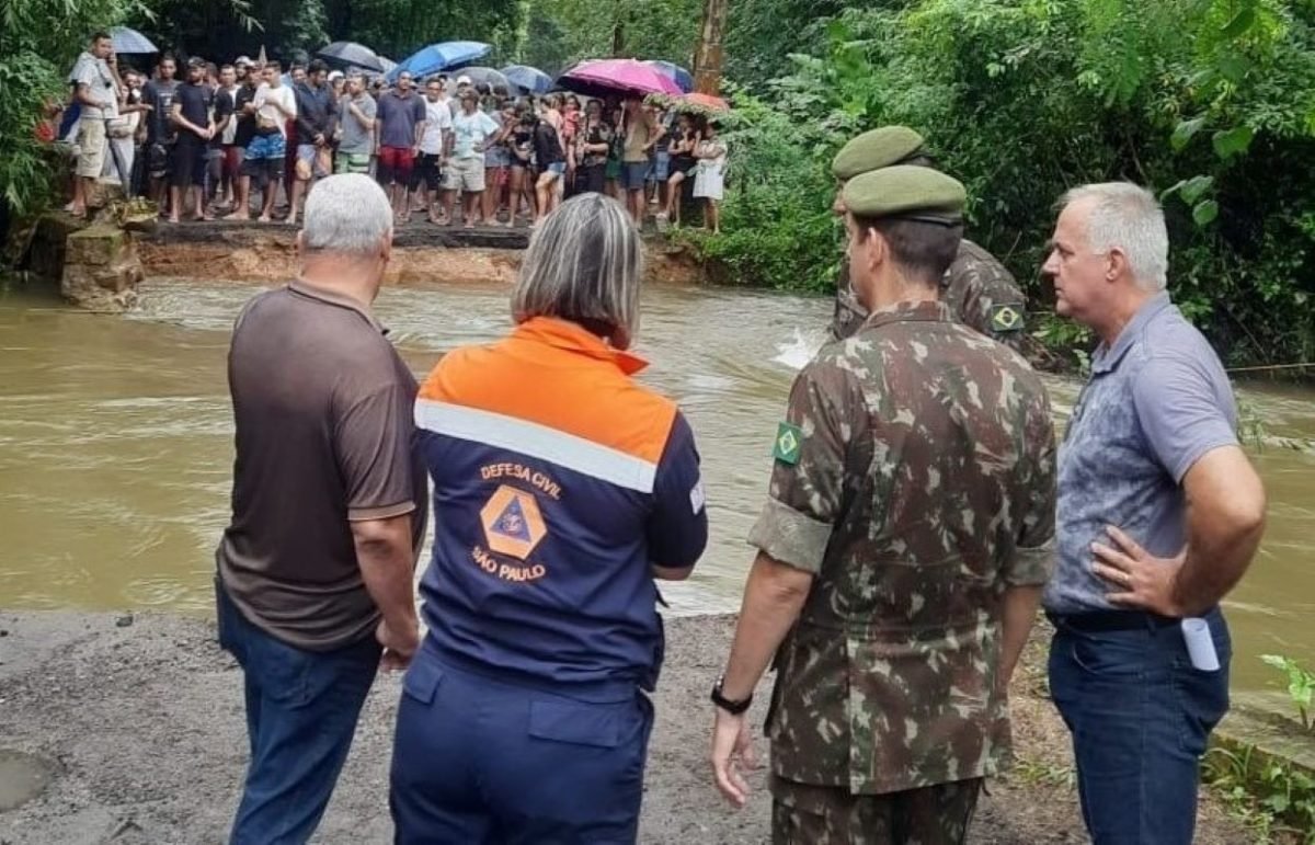 Cinco pessoas observam e conversam entre si enquanto dezenas de cidadãos estão do outro lado do rio curiosos