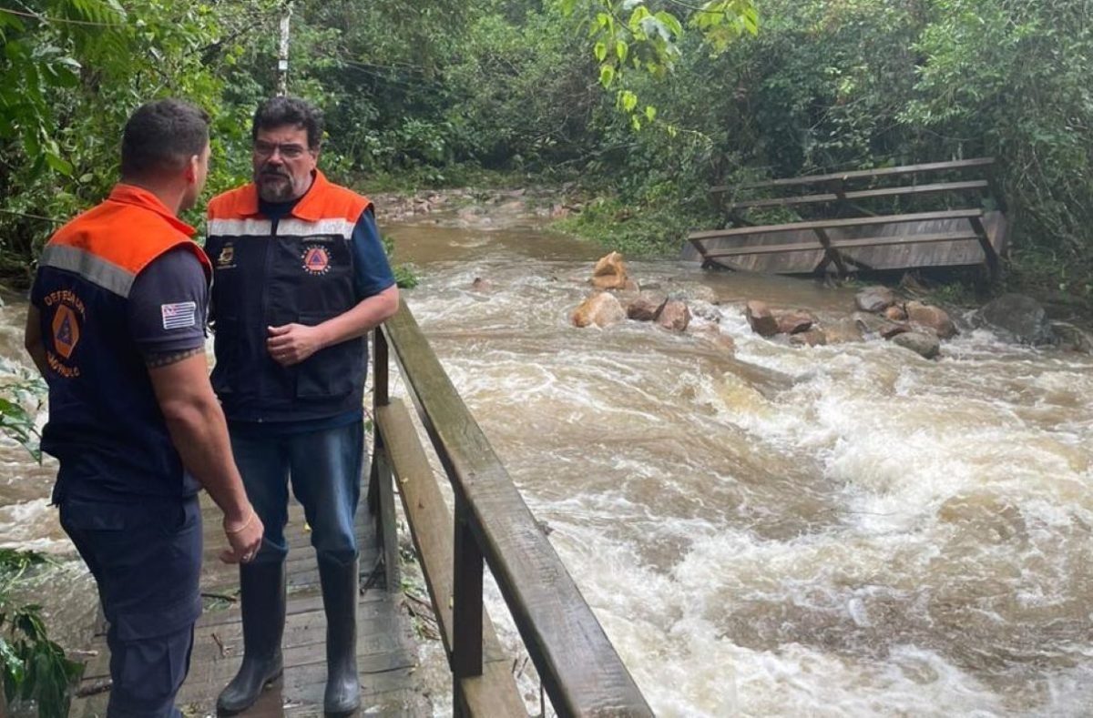 Dois homens em cima de uma estrutura de madeira enquanto uma correnteza de água passa ao lado