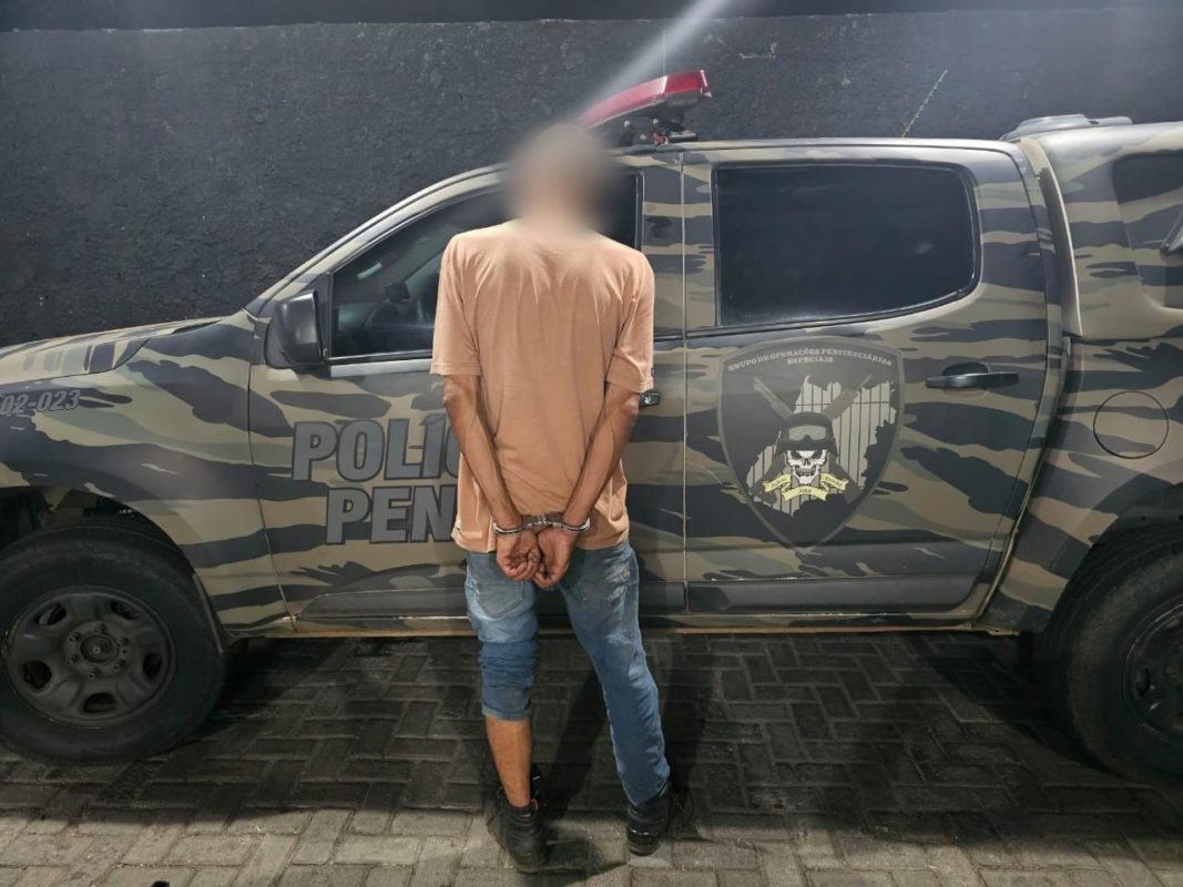 Imagem colorida de um homem de costas e de frente para um camburão da Polícia Penal de GO - Metrópoles