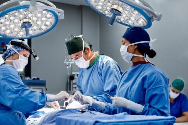 Imagem colorida de cirurgiã operando paciente na sala de emergência