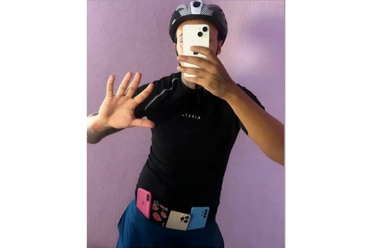 Foto colorida de homem cobrindo rosto com celular e com quatro aparelhos semelhantes na cintura - Metrópoles