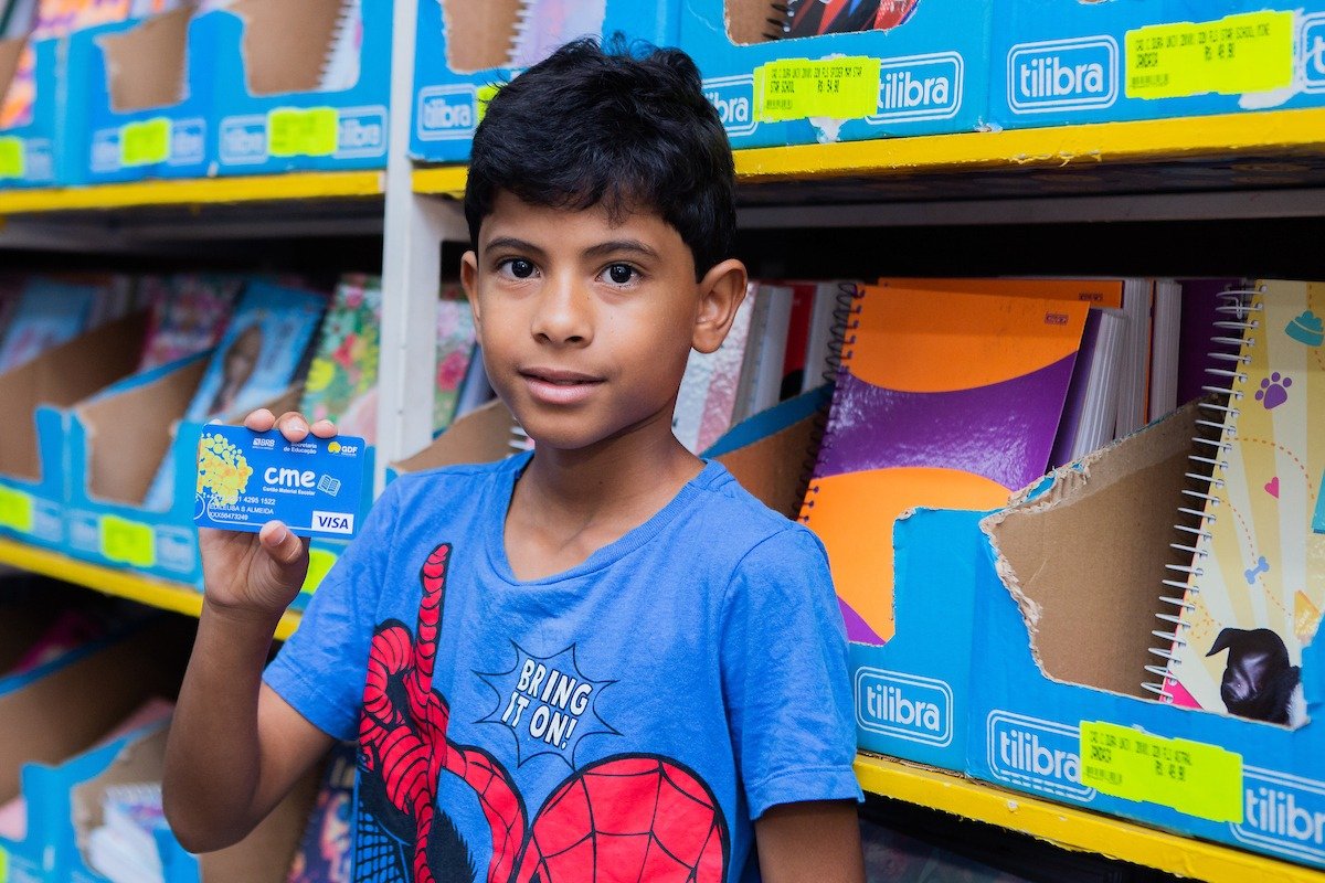 Fotografia colorida de um garoto com o Cartão Material Escolar