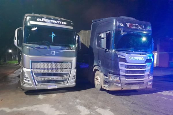 Imagem colorida de dois caminhões de carga, parados, à noite