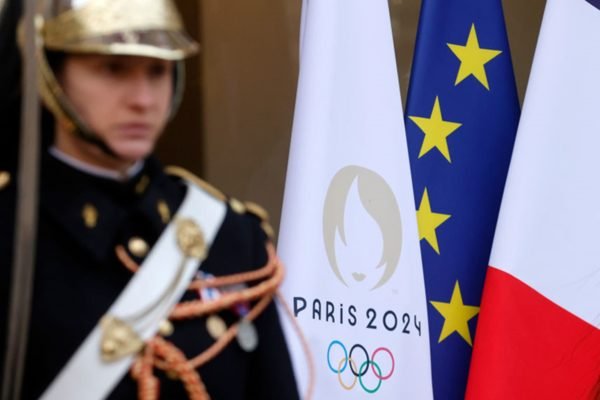 Imagem colorida de guarda ao lado da bandeira das Olimpíadas - Metrópoles
