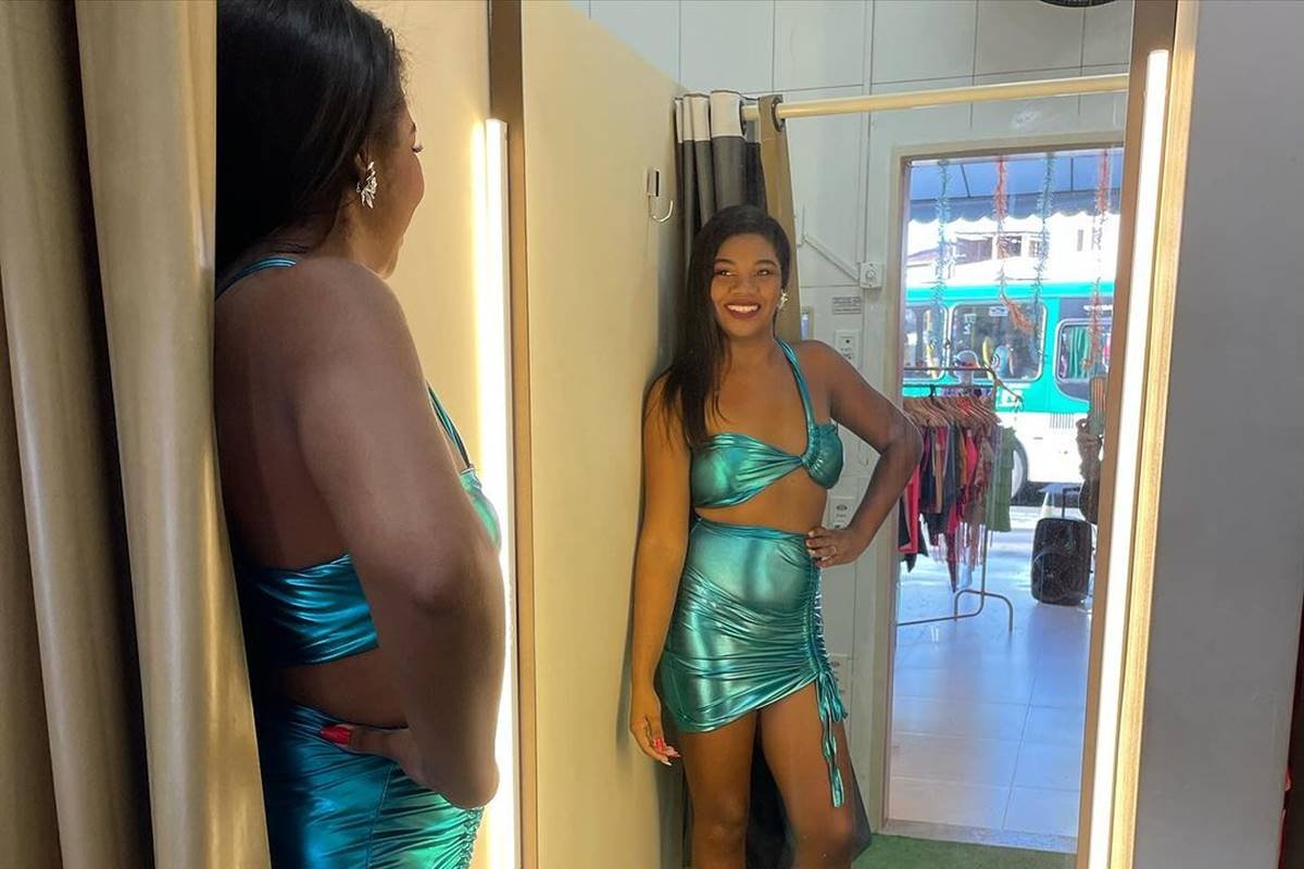 foto colorida de mulher negra de top e saia azul se olhando em espelho - metrópoles