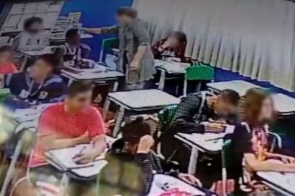 Imagem de sala de aula cheia de alunos; uma professora encosta na testa de um aluno - Metrópoles