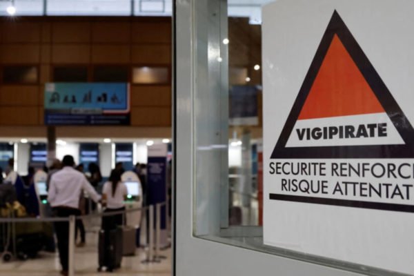 Imagem colorida de passageiros em fila para fazer o check-in ao lado de uma placa de advertência Vigipirate (à direita) que diz "segurança reforçada, risco de ataque terrorista" no aeroporto internacional de Caiena, Guiana Francesa, em 24 de março de 2024 França - Metrópoles