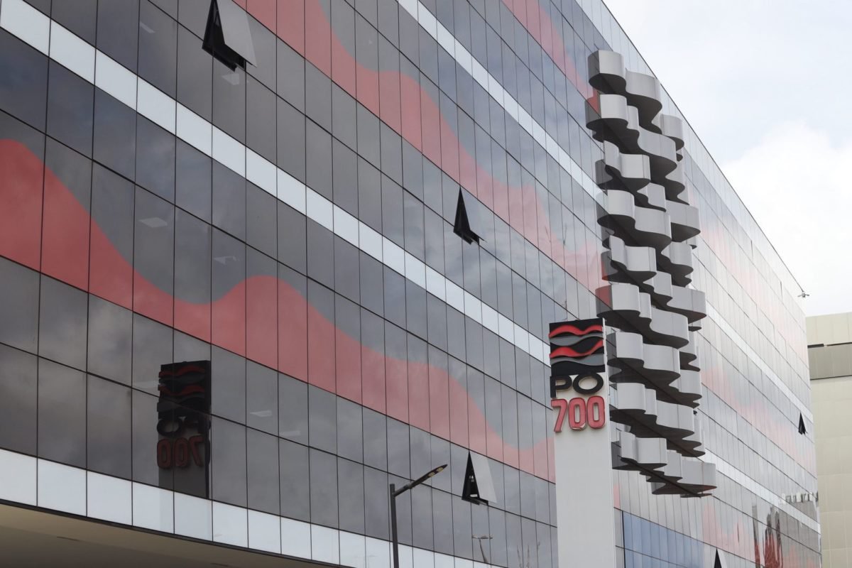 Foto colorida de fachada de prédio vermelho e prédio com placa escrito PO 700
