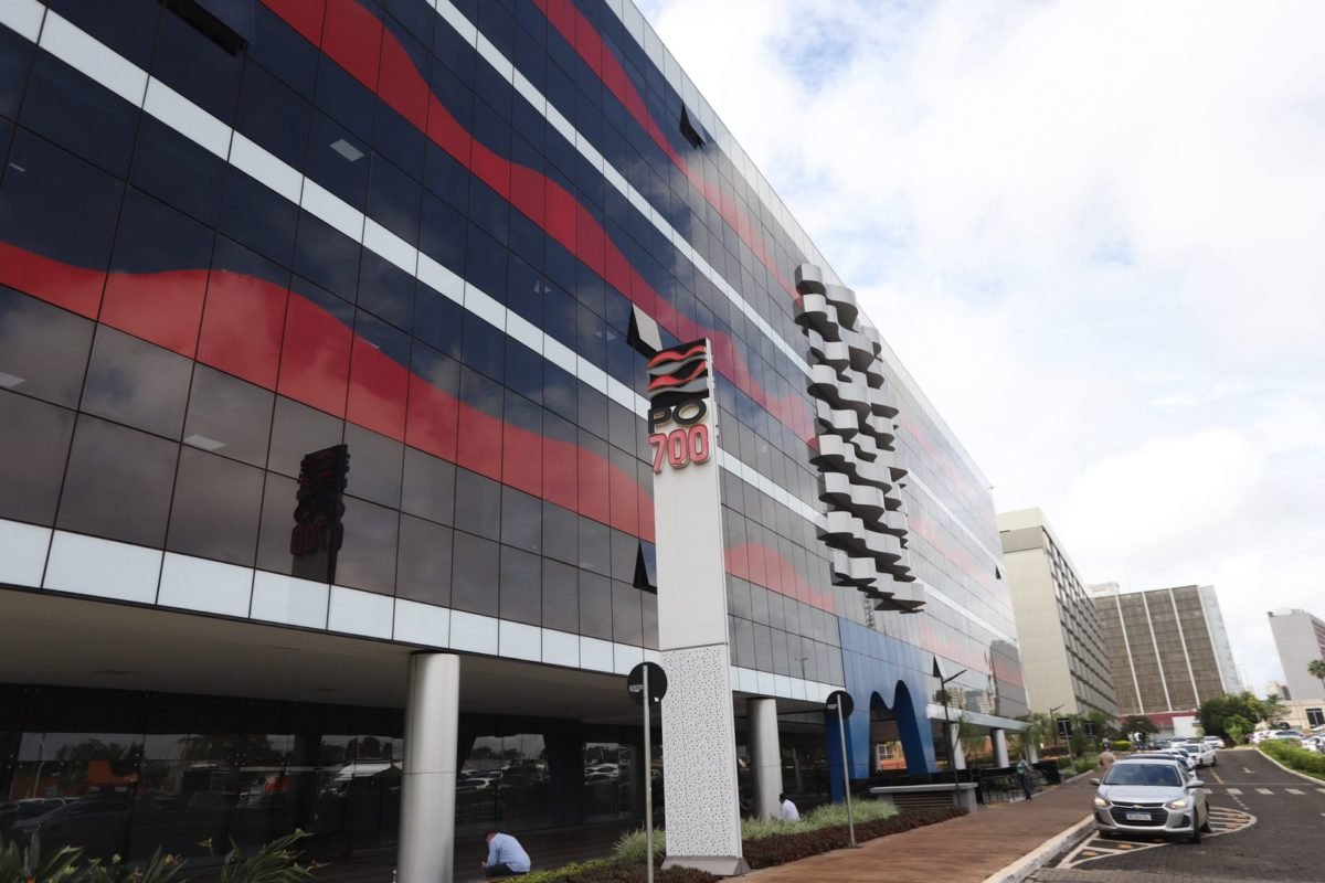 Foto colorida de fachada de prédio vermelho e prédio com placa escrito PO 700