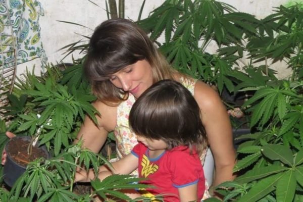 Imagem colorida mostra Angela Aboin e sua filha, diagnosticada com Transtorno do Espectro Autista (TEA), em meio a várias plantas de cannabis; Justiça a autorizou cultivar a planta em casa - Metrópoles