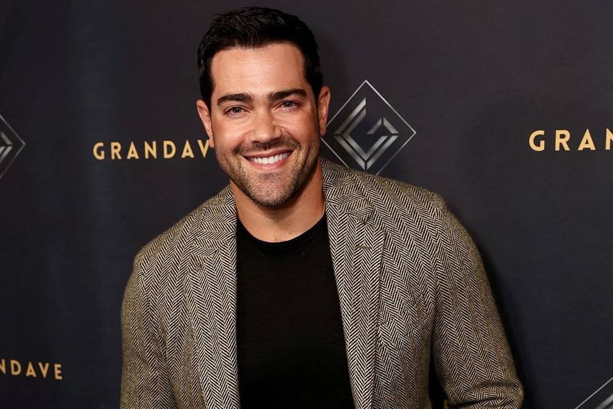 foto colorida de homem branco sorrindo e vestido com blusa preta e blazer marrom - metrópoles