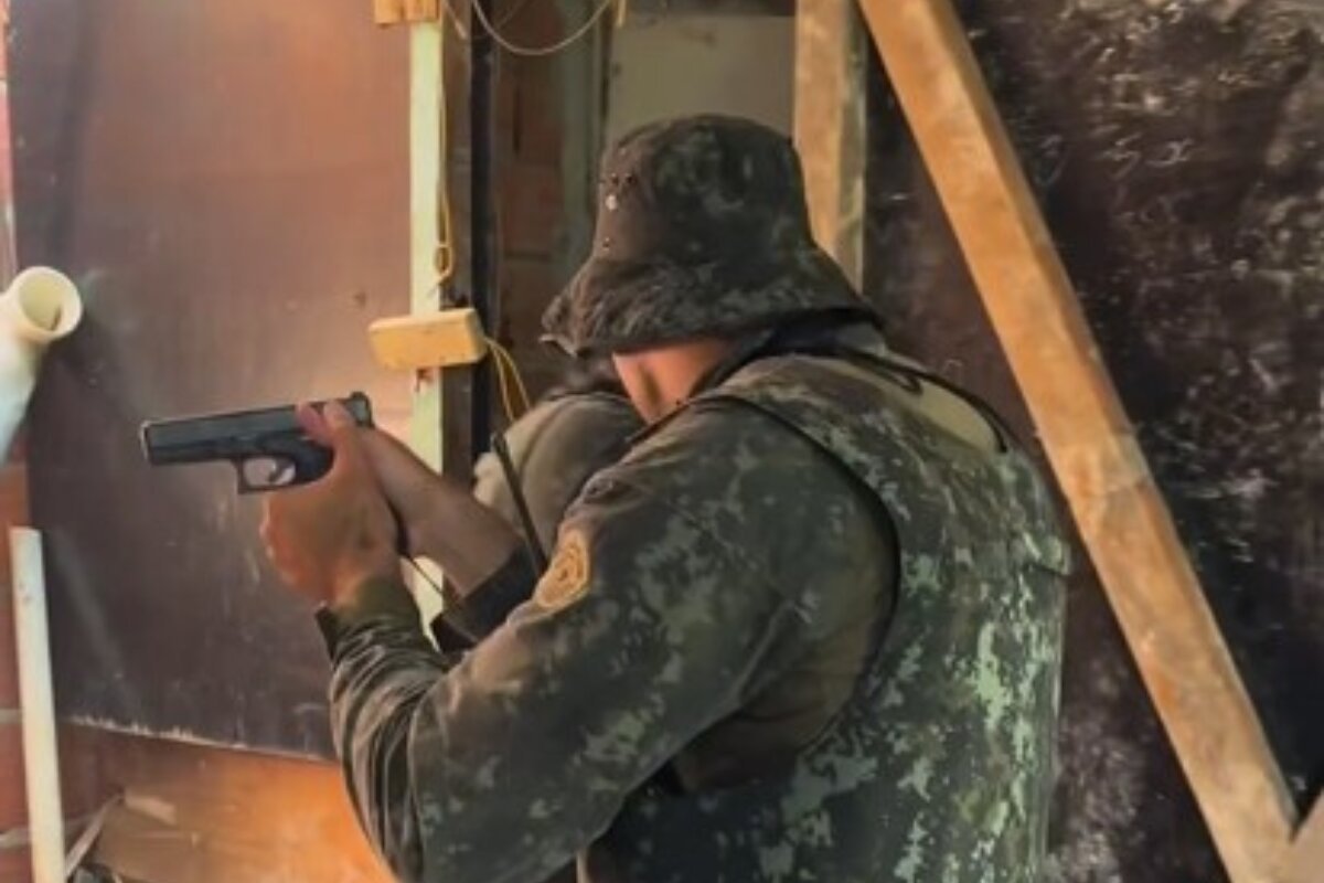 Foto colorida de policial militar, com roupa camuflada, empunhando pistola - Metrópoles