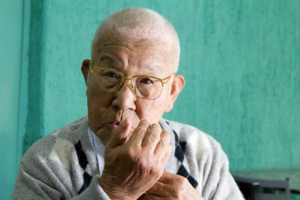 imagem colorida mostra homem de cabelos brancos. ele usa óculos e é japonês.