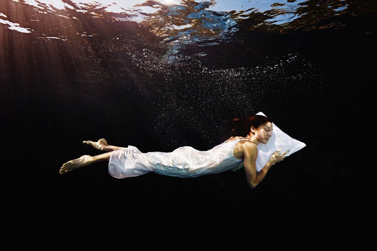 Mulher de camisola com a cabeça no travesseiro dormindo debaixo d'água. Conceito de sonhar. Metrópoles