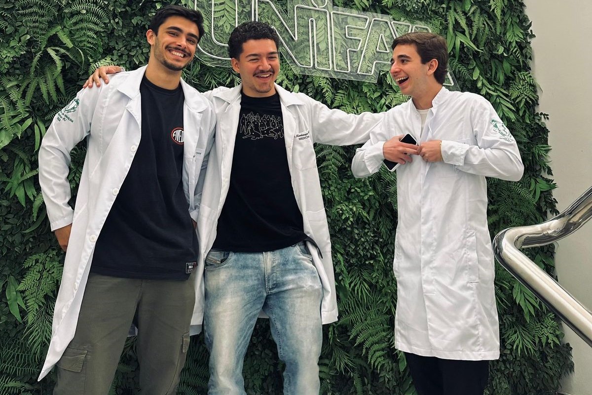 Foto do personagem Guilherme junto a mais 2 amigos do curso de medicina. Eles usam jaleco. Metrópoles