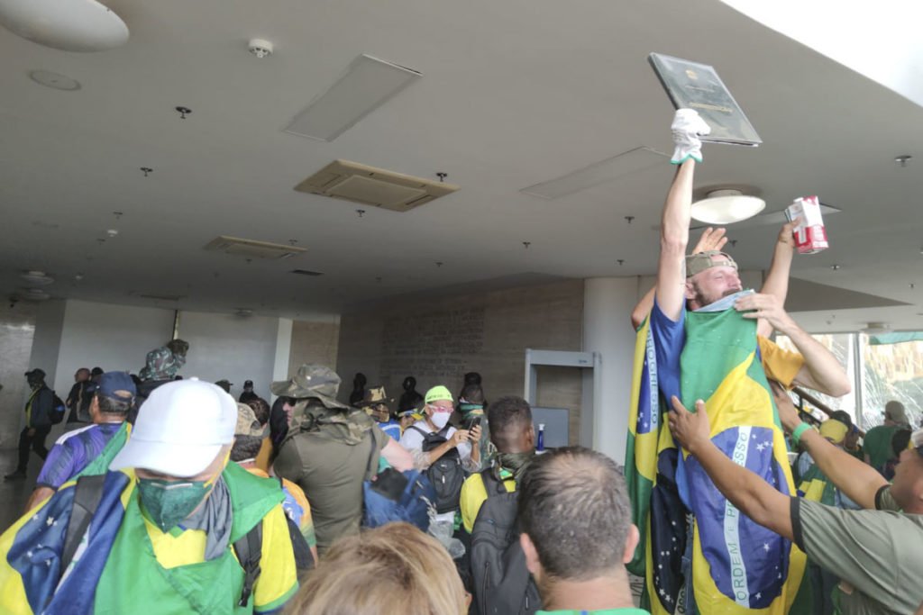 Manifestantes bolsonaristas invadem e destroem o prédio do Supremo Tribunal Federal (STF). Os terroristas andam pelo ambiente interno e um deles, de pé, segura um exemplar da Constituição Federal - Metrópoles